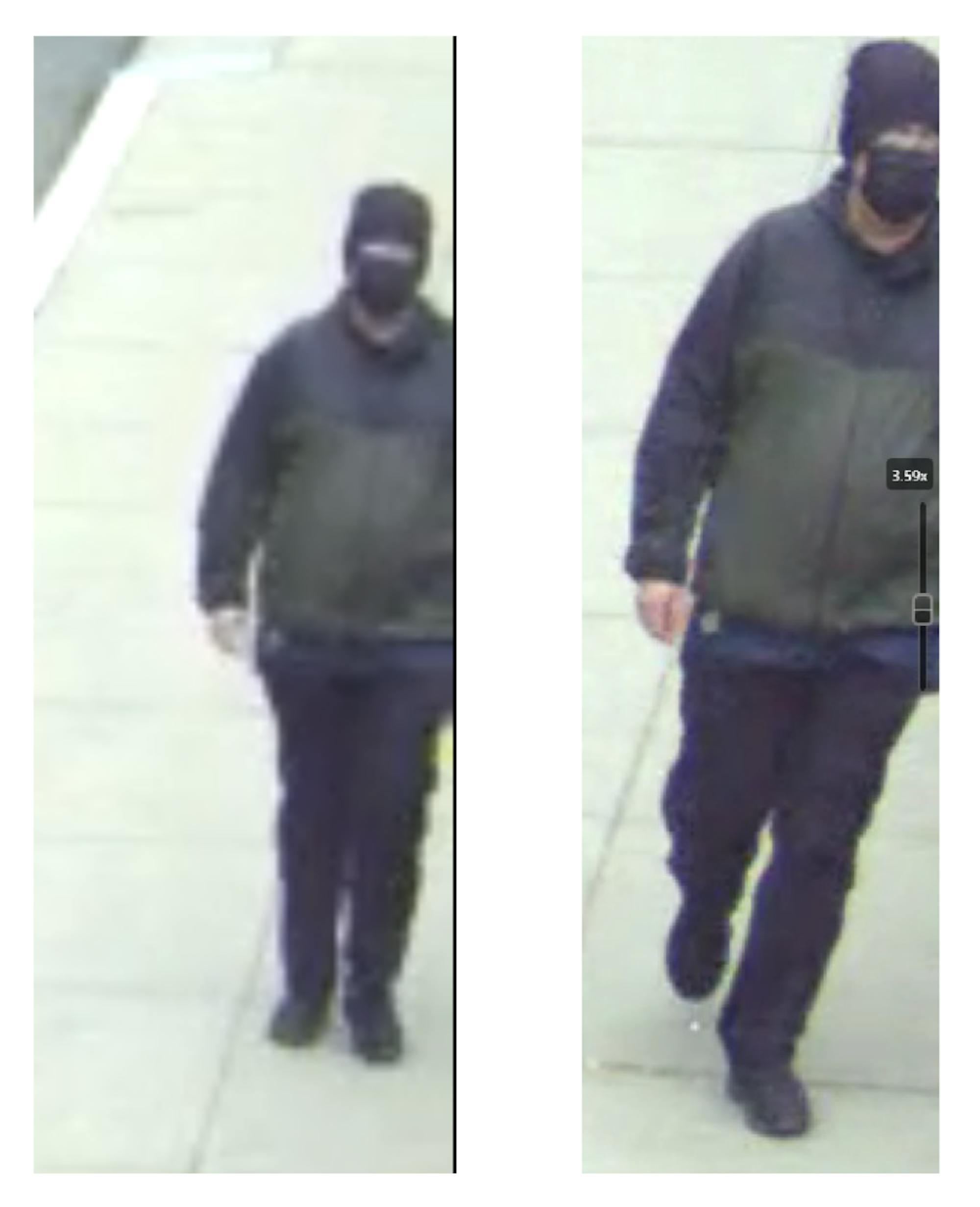 A man in dark clothing with his face covered walks along a sidewalk with nothing visible in the background.