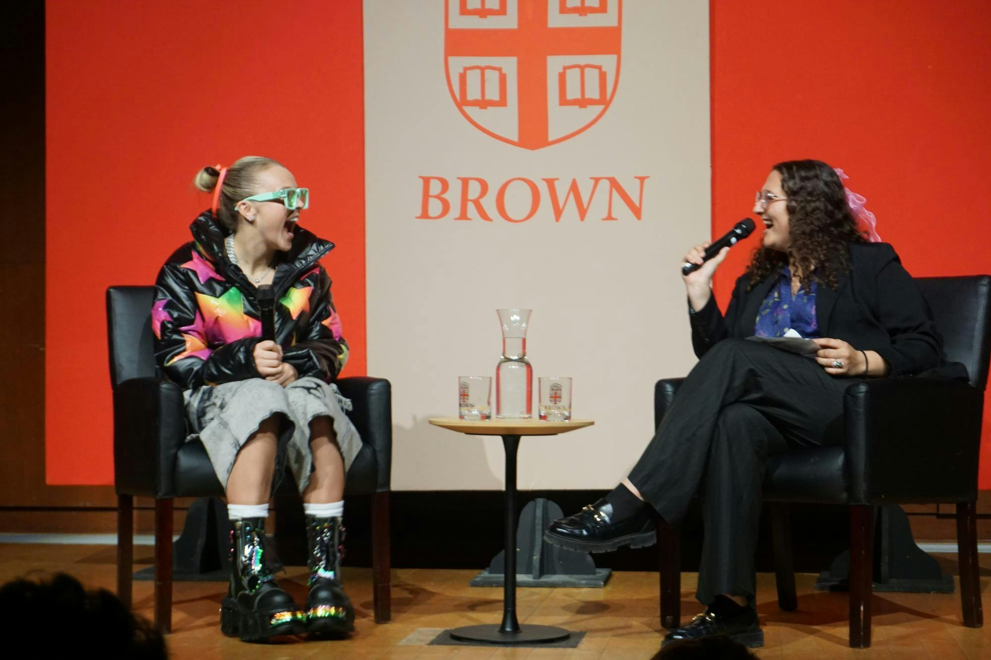 JoJo Siwa sits with a moderator in front of a red Brown University logo.