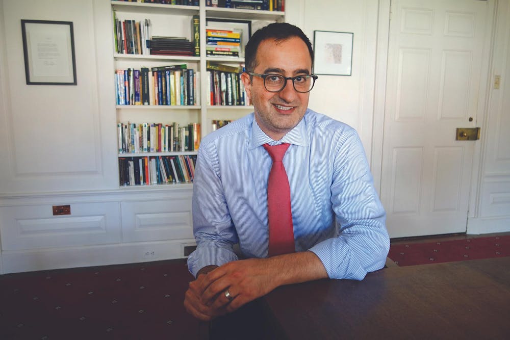 Rashid Zia, wearing glasses, a blue pinstripe shirt and a red tie, smiles at the camera in front of a wall lined with books.