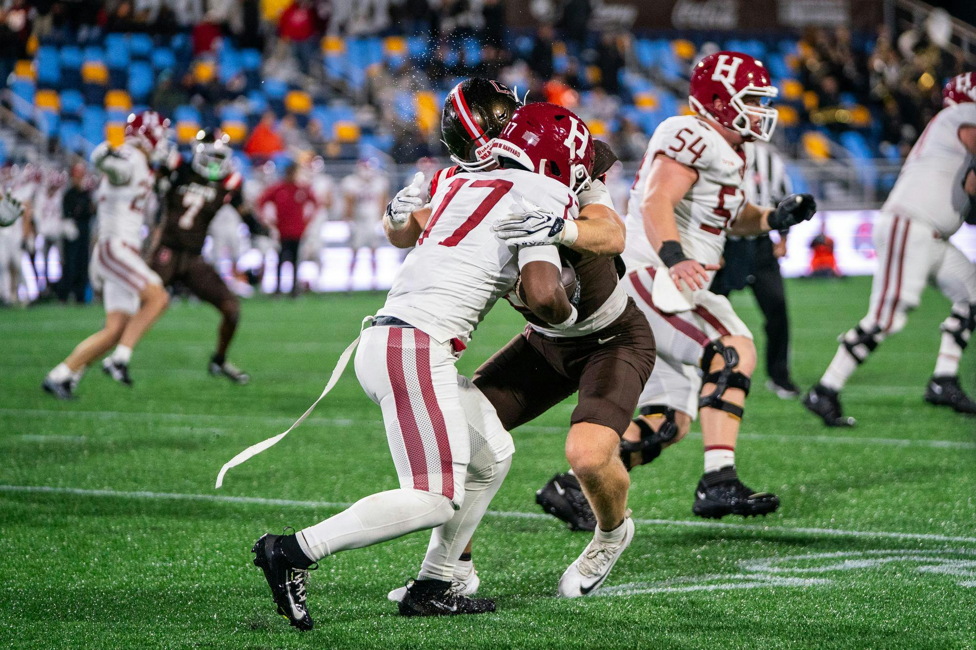 A photo of a Harvard football player colliding with a Brown player. Other players run past them in the background. 