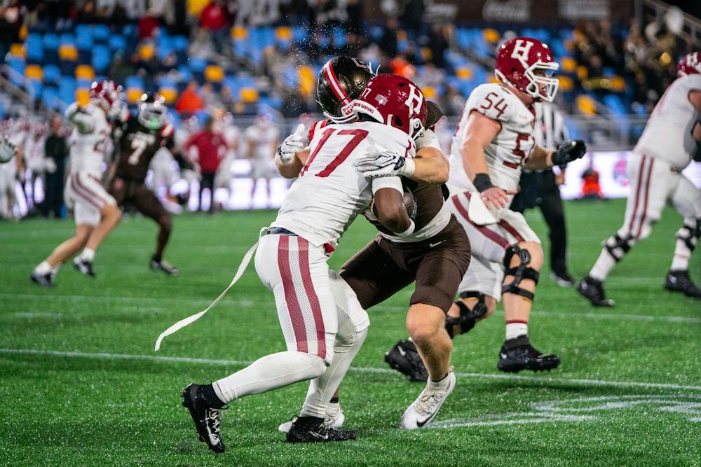 A photo of a Harvard football player colliding with a Brown player. Other players run past them in the background. 