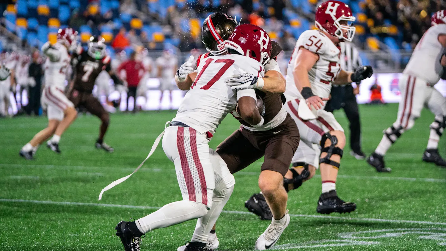 A photo of a Harvard football player colliding with a Brown player. Other players run past them in the background.