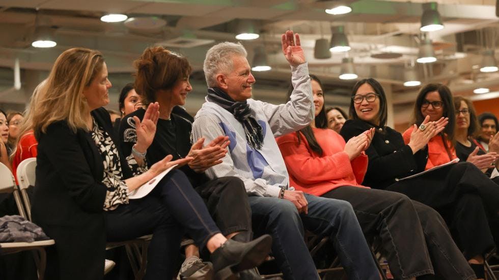 An image of a row of people in a crowd, with a man raising his hand and people around him clapping.