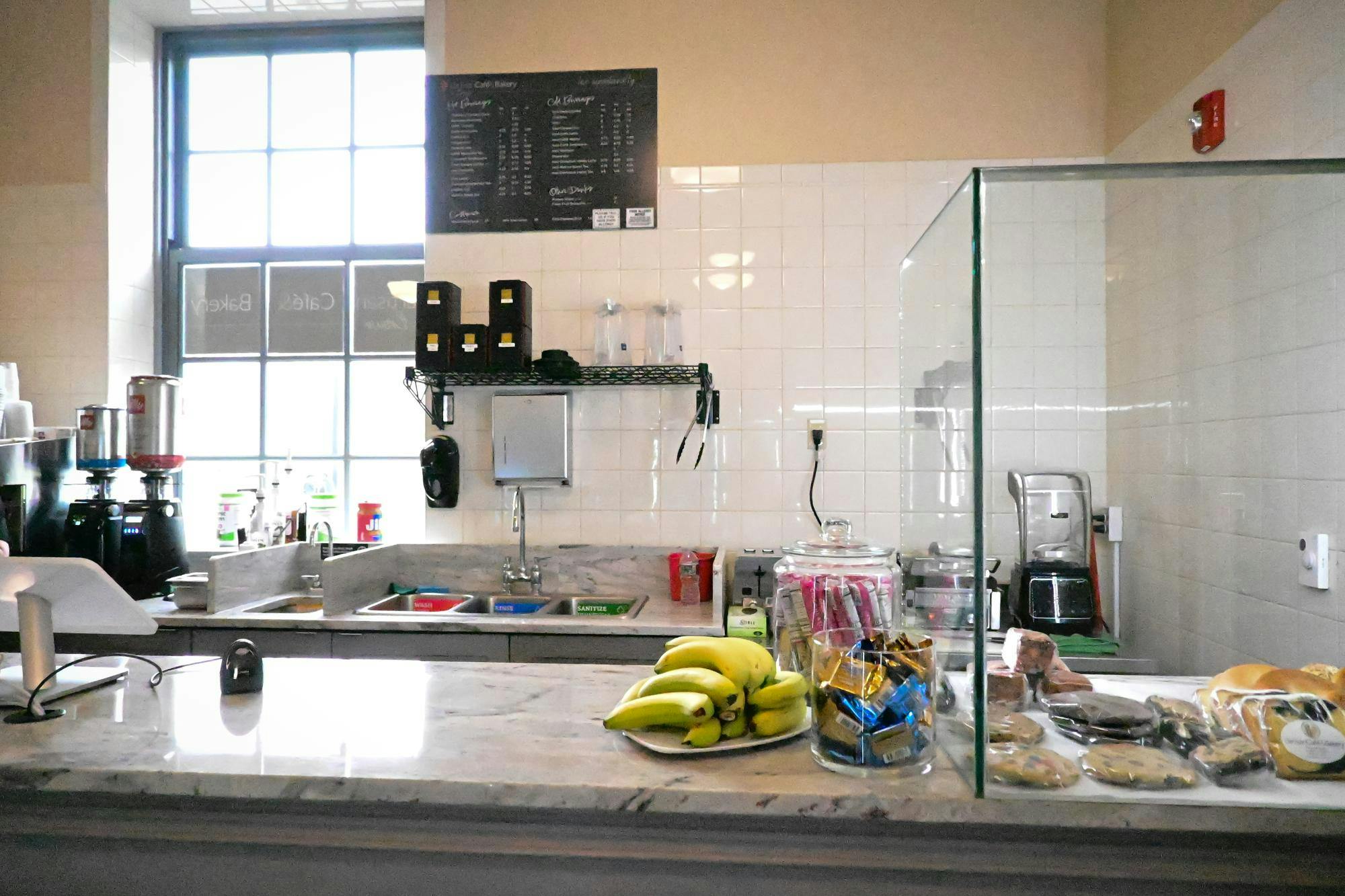 A white-tiled room with a white marble countertop adorned with pastries and fruit and black chalkboard on the wall.