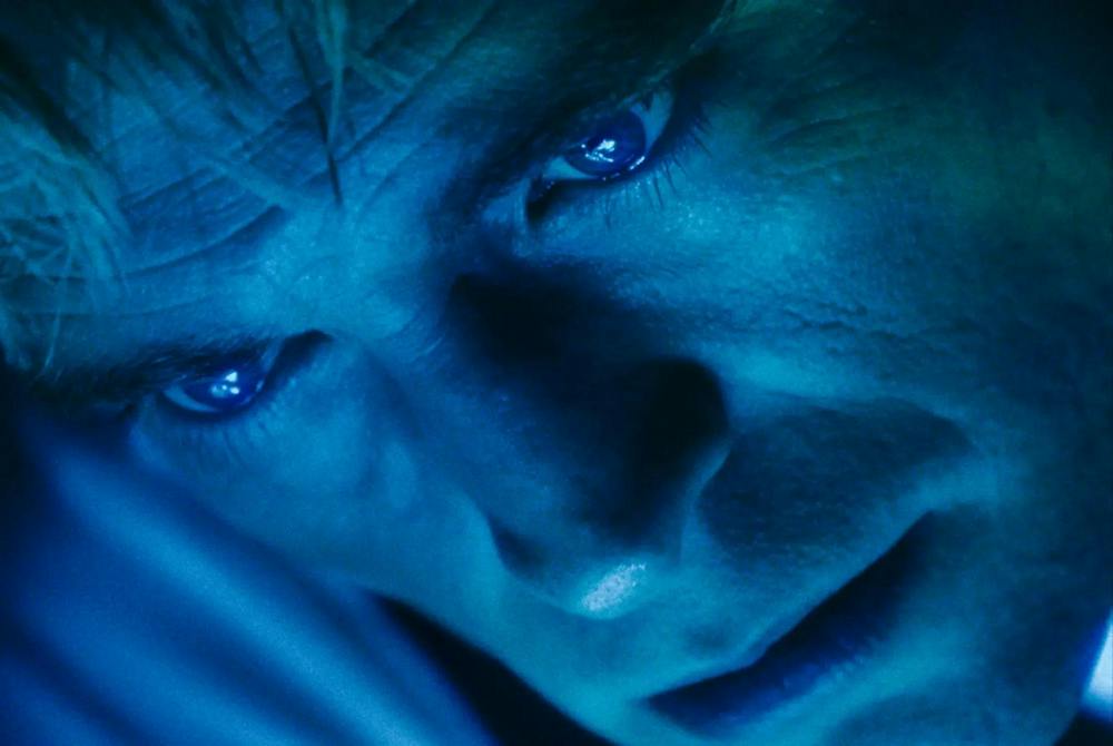 A still from Primetime, capturing Robert Pattinson as he stares at a blue screen, his face illuminated by its reflection.
