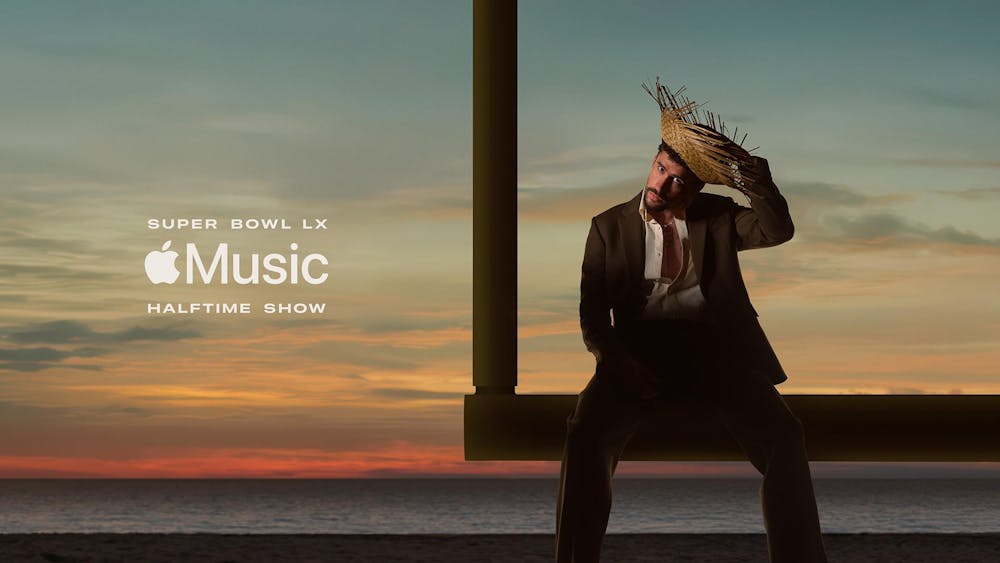A photo of Bad Bunny, donning a pava and brown suit, sitting atop a football goalpost in front of a sunset on a beach. Over the photo, white text reads "Super Bowl LX" above the Apple Music logo and additional text reading "Halftime show."