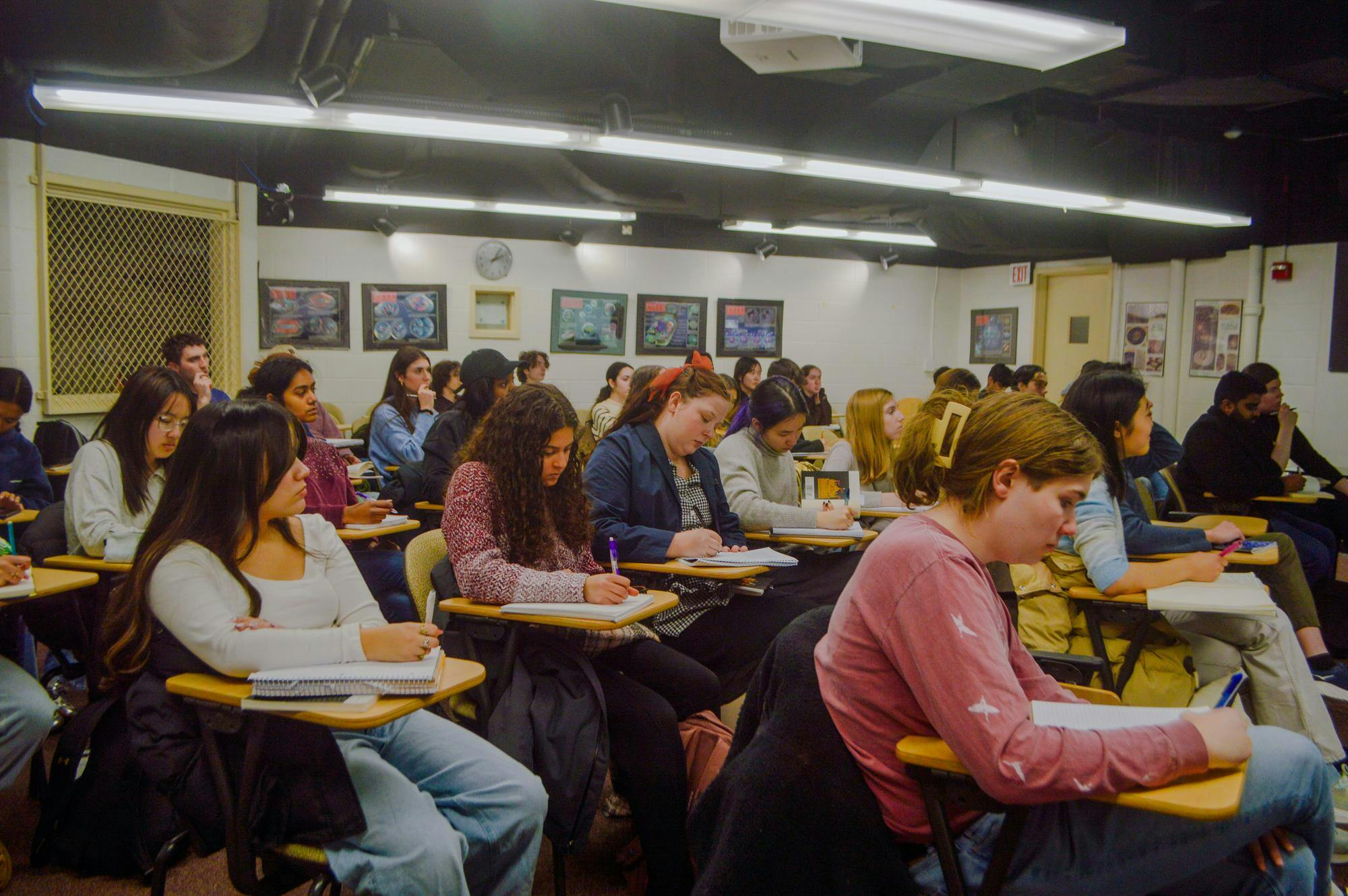 Picture of students in a classroom taking notes in their notebooks without the use of technology. There is no technology visible in the image.