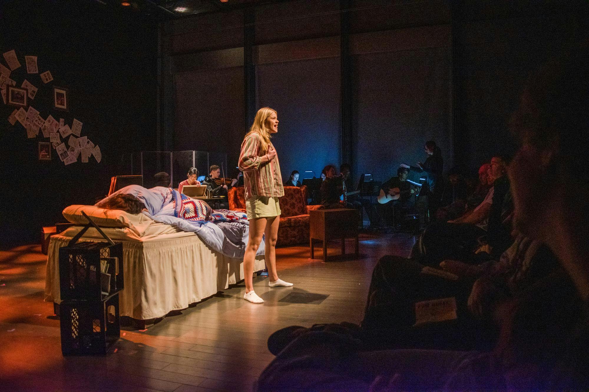 A photo of Dylan George ‘29, playing Medium Alison, singing into the crowd with a bed behind her.