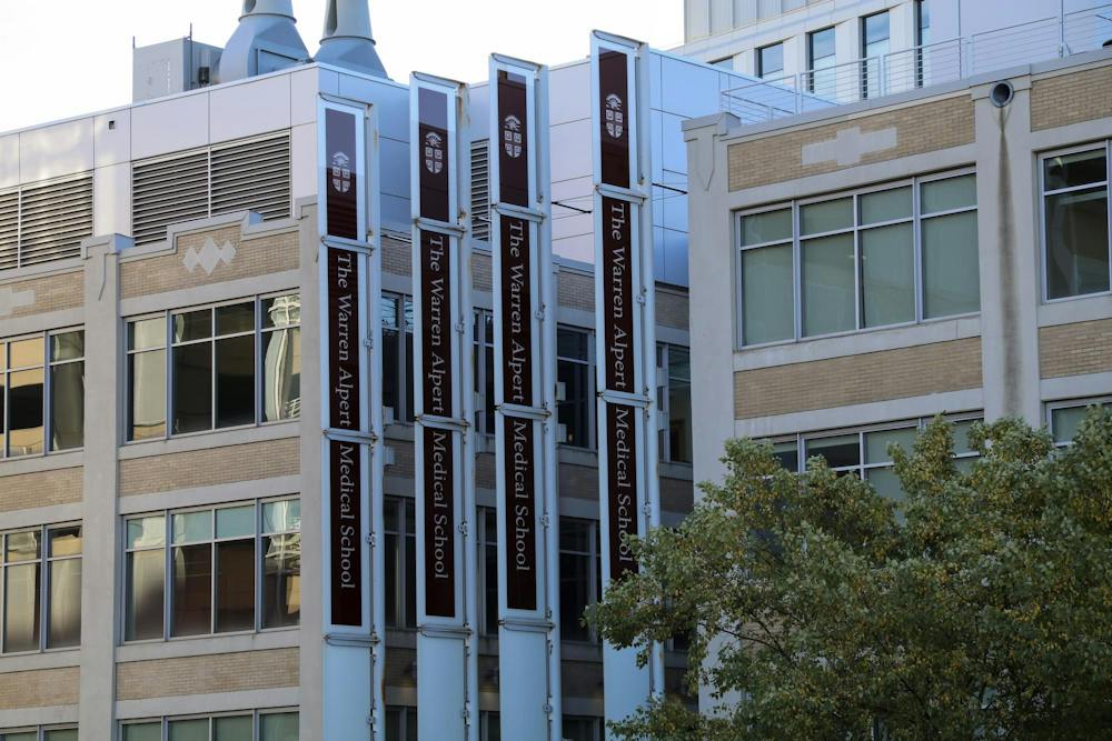 A photo of The Warren Alpert Medical School, two large beige buildings with four signs that read “The Warren Alpert Medical School.”