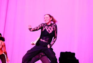 A dancer in front of a pink background extending one arm out with palm facing the audience.