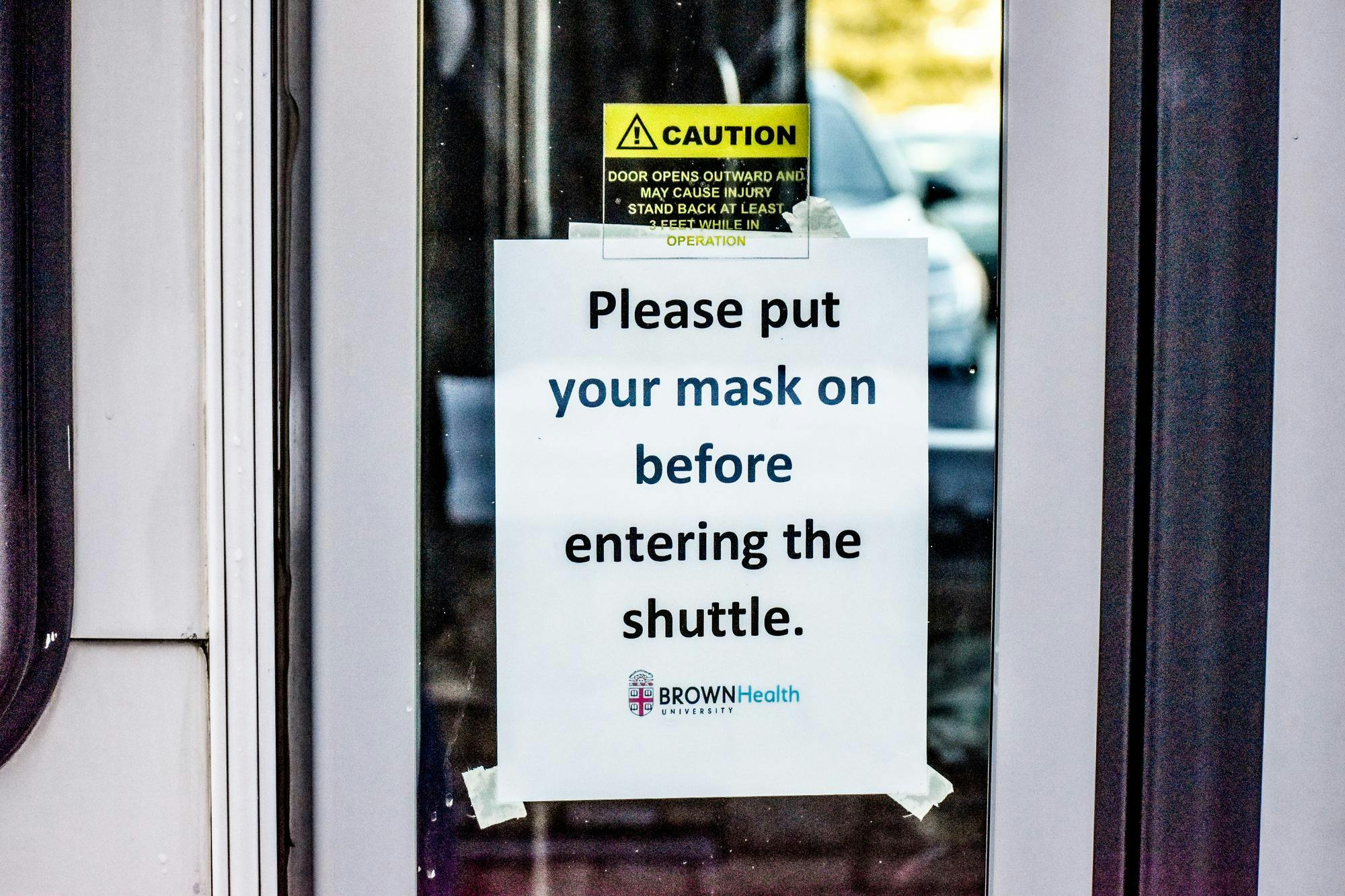A sign on the door to a  University shuttle bus reads, "Please put a mask on before entering the shuttle."