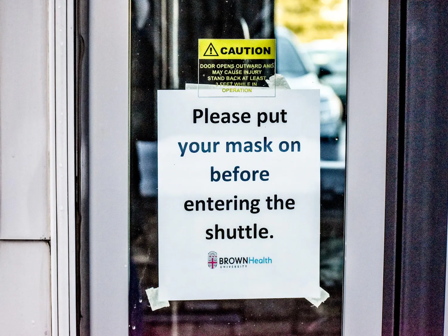 A sign on the door to a University shuttle bus reads, "Please put a mask on before entering the shuttle."