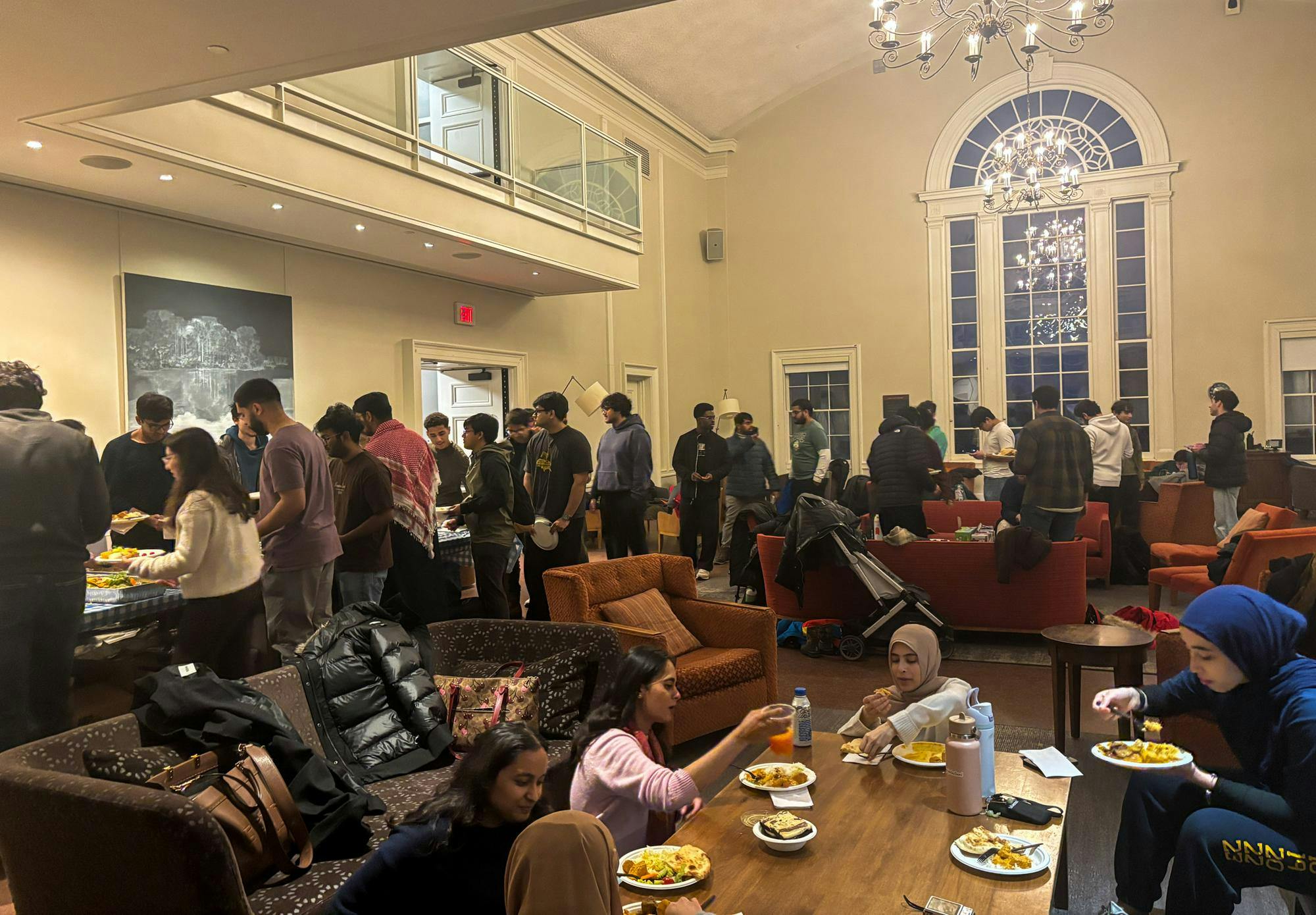 Many students in the Leung Gallery stand in line and sit in couches while eating food.