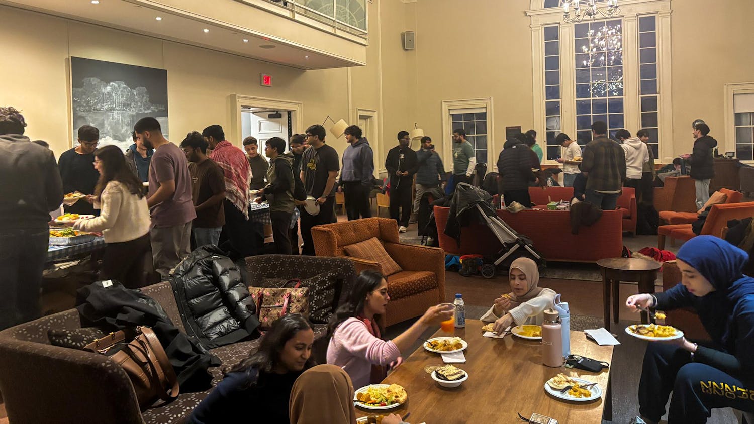 Many students in the Leung Gallery stand in line and sit in couches while eating food.