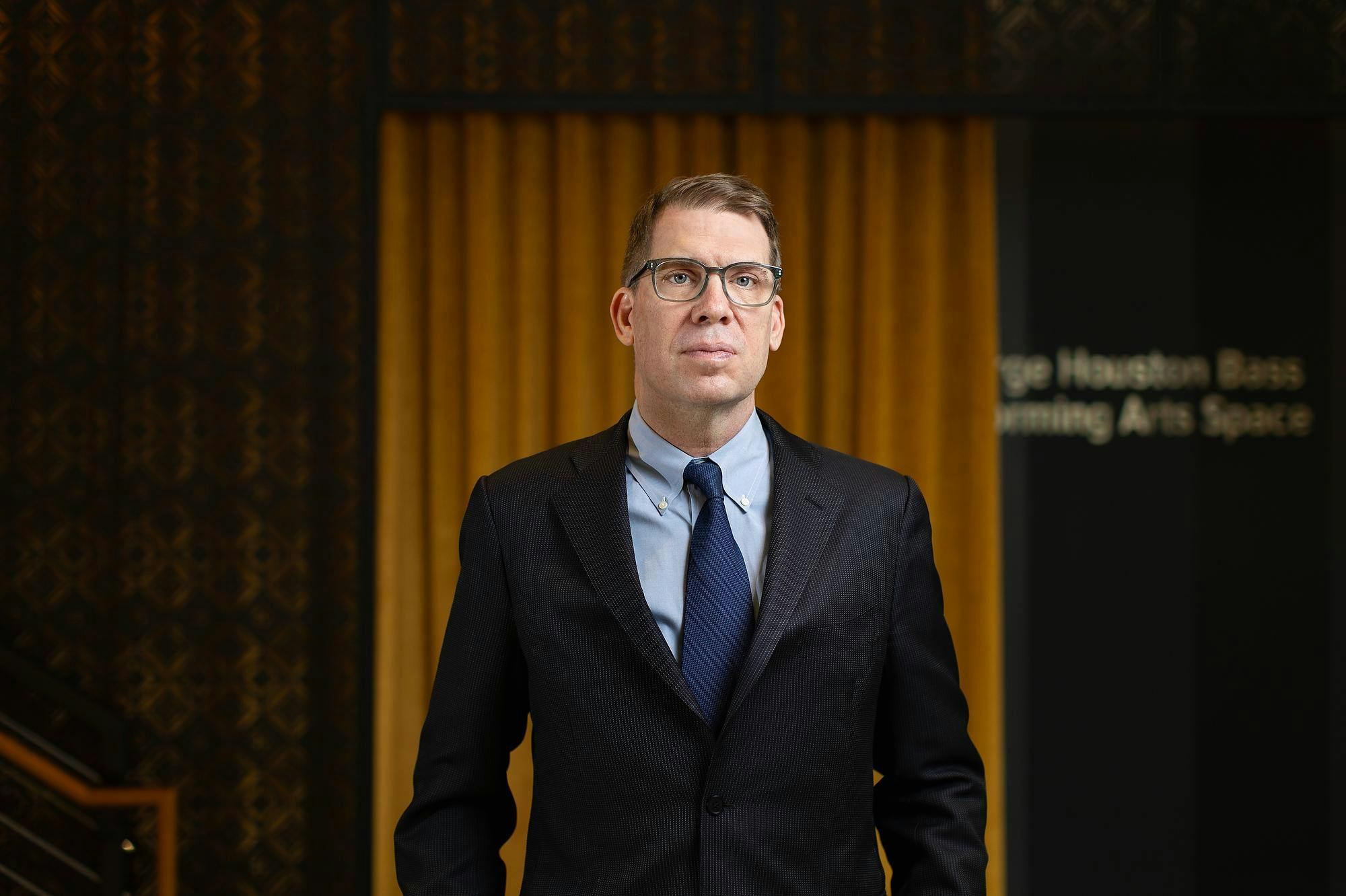 Matthew Guterl stands wearing a black blazer, light blue shirt and blue tie