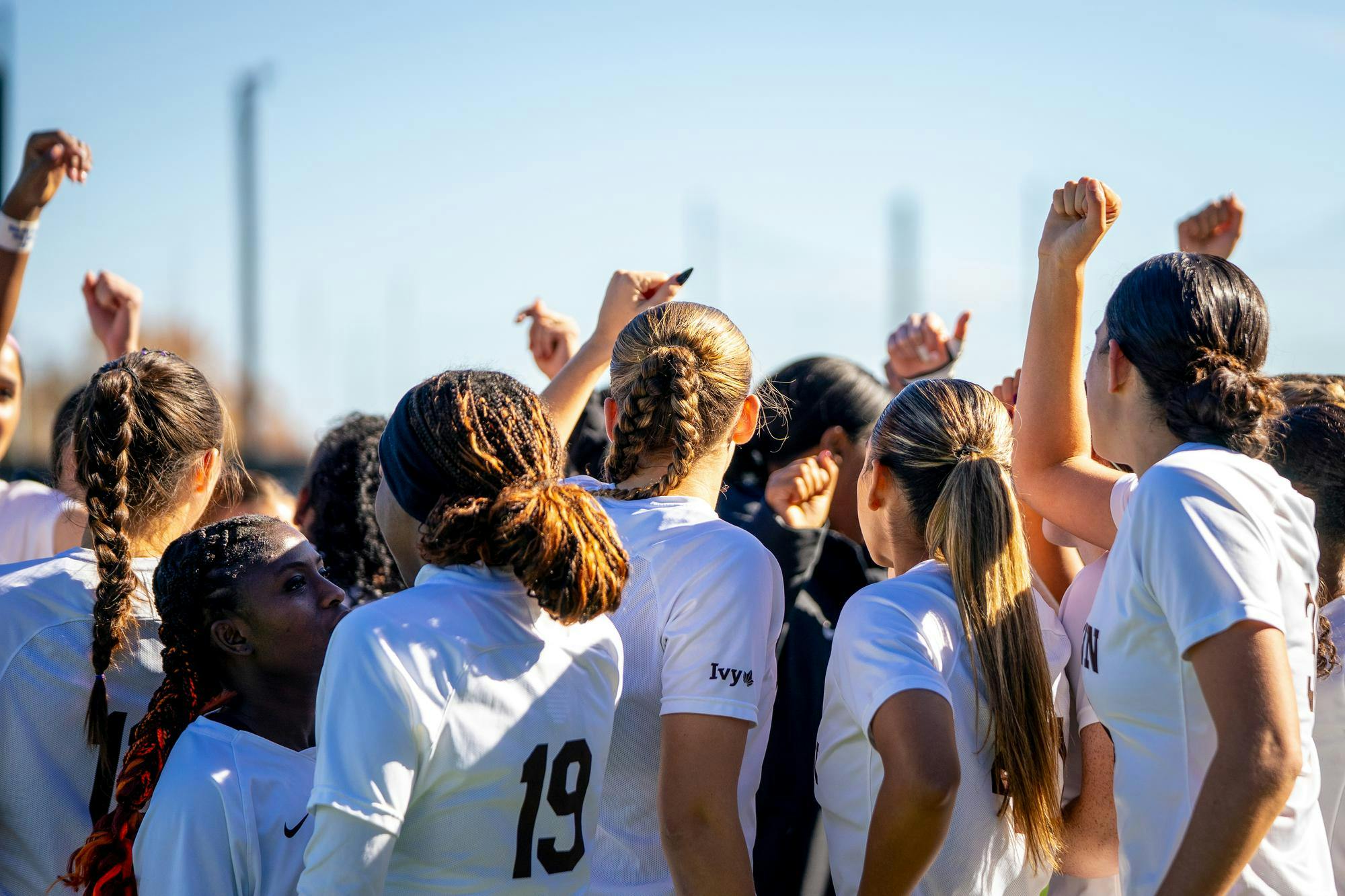 Photograph of a group of girls wearing white jerseys in a huddle.