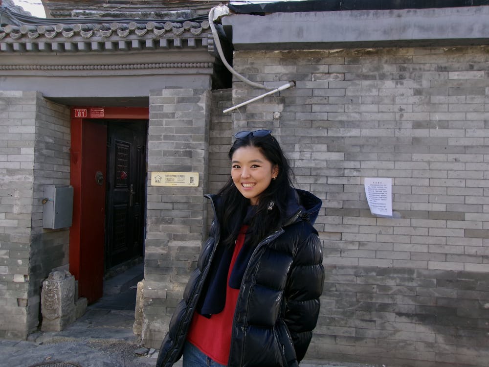 Woman standing in front of building wearing red sweater and black jacket. 