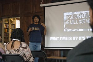 A member of the Beta Omega Chi fraternity is standing in the front of the room speaking. There is a slide behind him that reads “What time is it?”