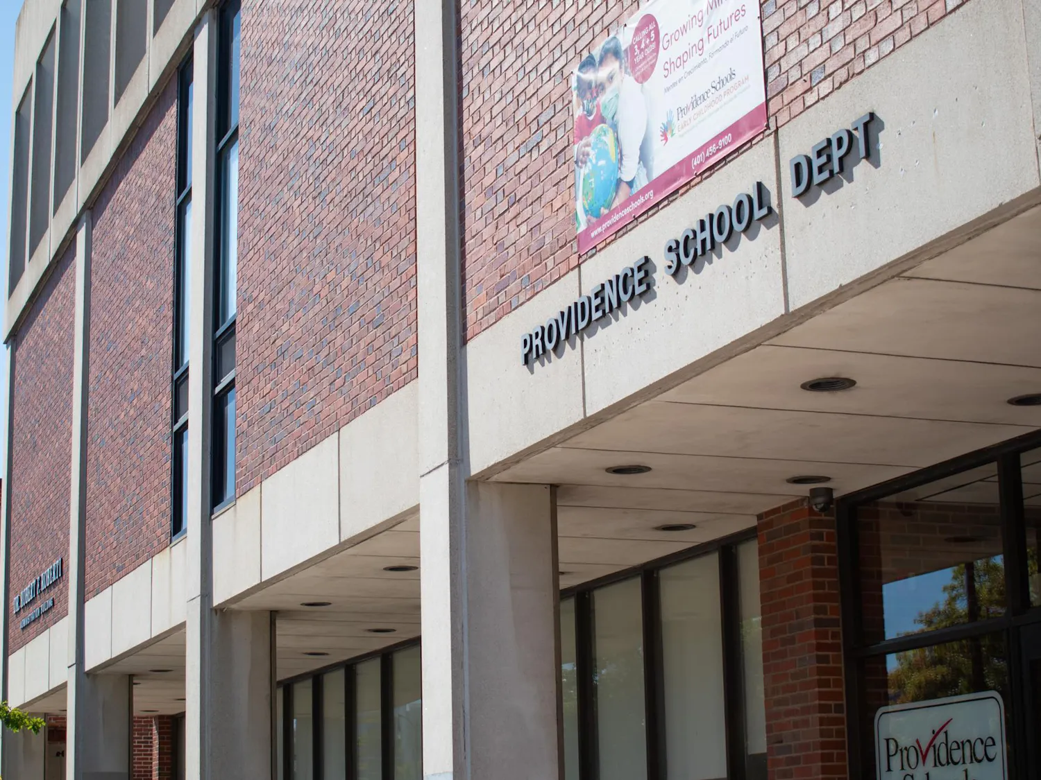 The Providence Public School Department building, a brick building with with words Providence School Dept on concrete on the building.