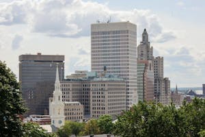 A view of downtown Providence from College Hill. The top of the First Baptist Church can be seen in the foreground, and larger buildings, like the Superman Building, stand behind it. 