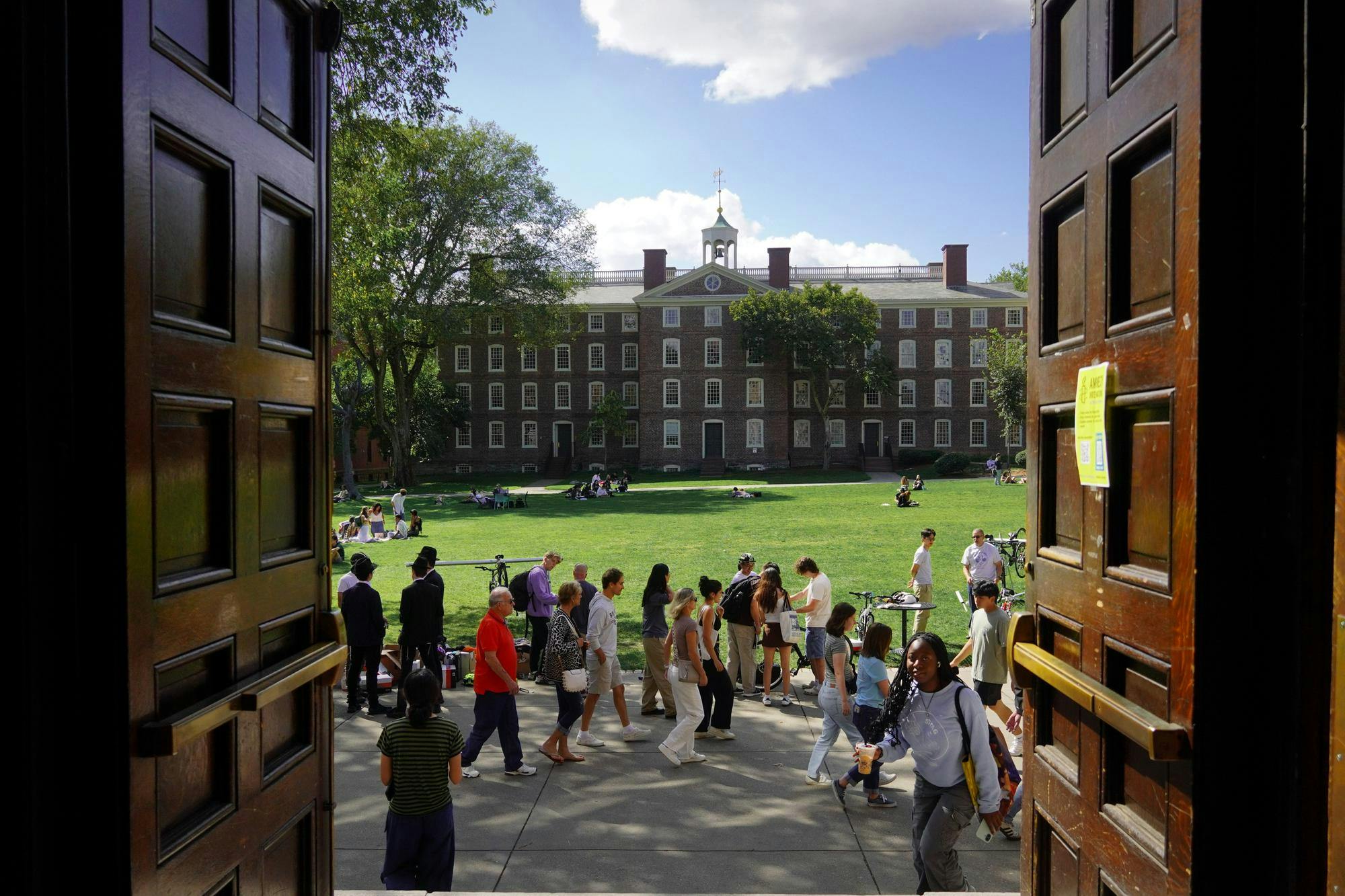 A picture of the Main Green at Brown University, which depicts students walking across the sidewalk and University Hall in the background. The picture is taken from the doors of Sayles Hall.