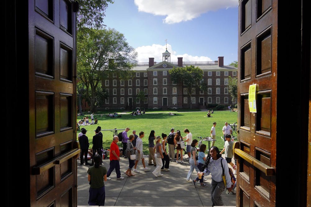 A picture of the Main Green at Brown University, which depicts students walking across the sidewalk and University Hall in the background. The picture is taken from the doors of Sayles Hall.