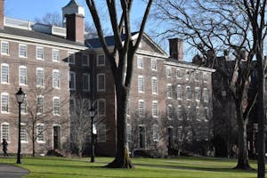University Hall, an old brick building, a sunny day, obstructed by a few bare trees.
