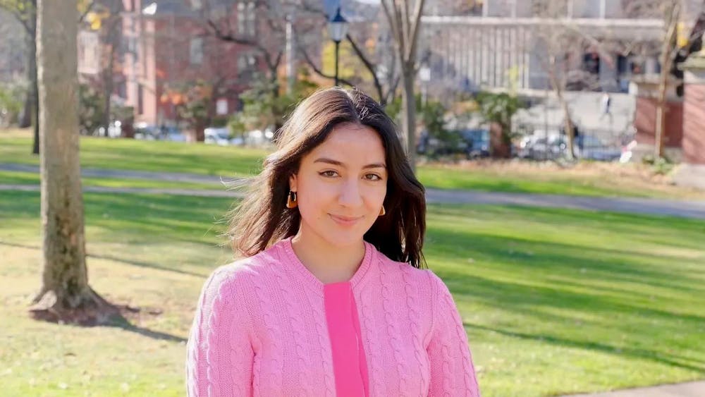 Palomo standing in the quiet green in the sun, in a pink sweater.