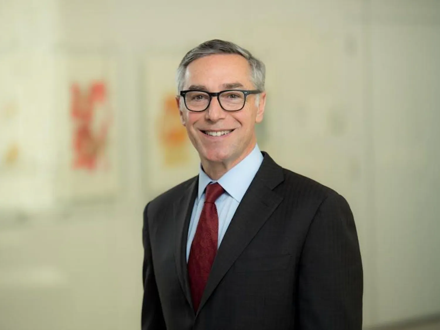 Richard Locke in a suit and tie standing in front of a blurry yellow background.