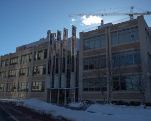 Photo of a long, rectangular building with large windows and four vertical brown banners displaying the words “Warren Alpert Medical School” in white text and the Brown University logo at the top. Some small piles of snow are in front of the building with a few bikes in front and on the bike rack.