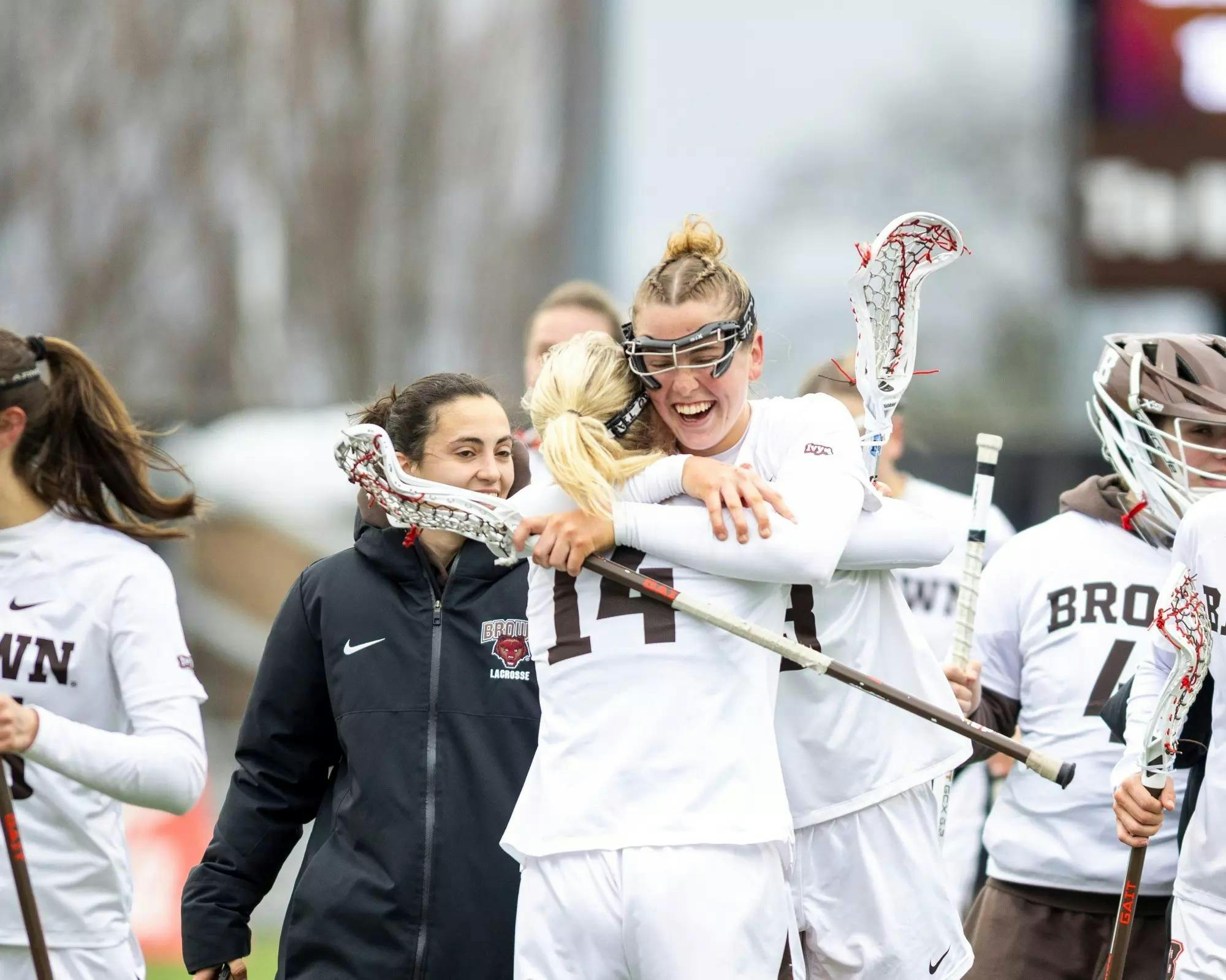 Two women's lacrosse players cheer and give each other a hug.