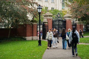 People walking next to the main green in front of the Van Wickle Gates