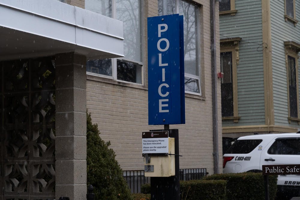 Photo of a blue vertical sign which reads "POLICE" in capital letters, with a building and a police car visible in the background.