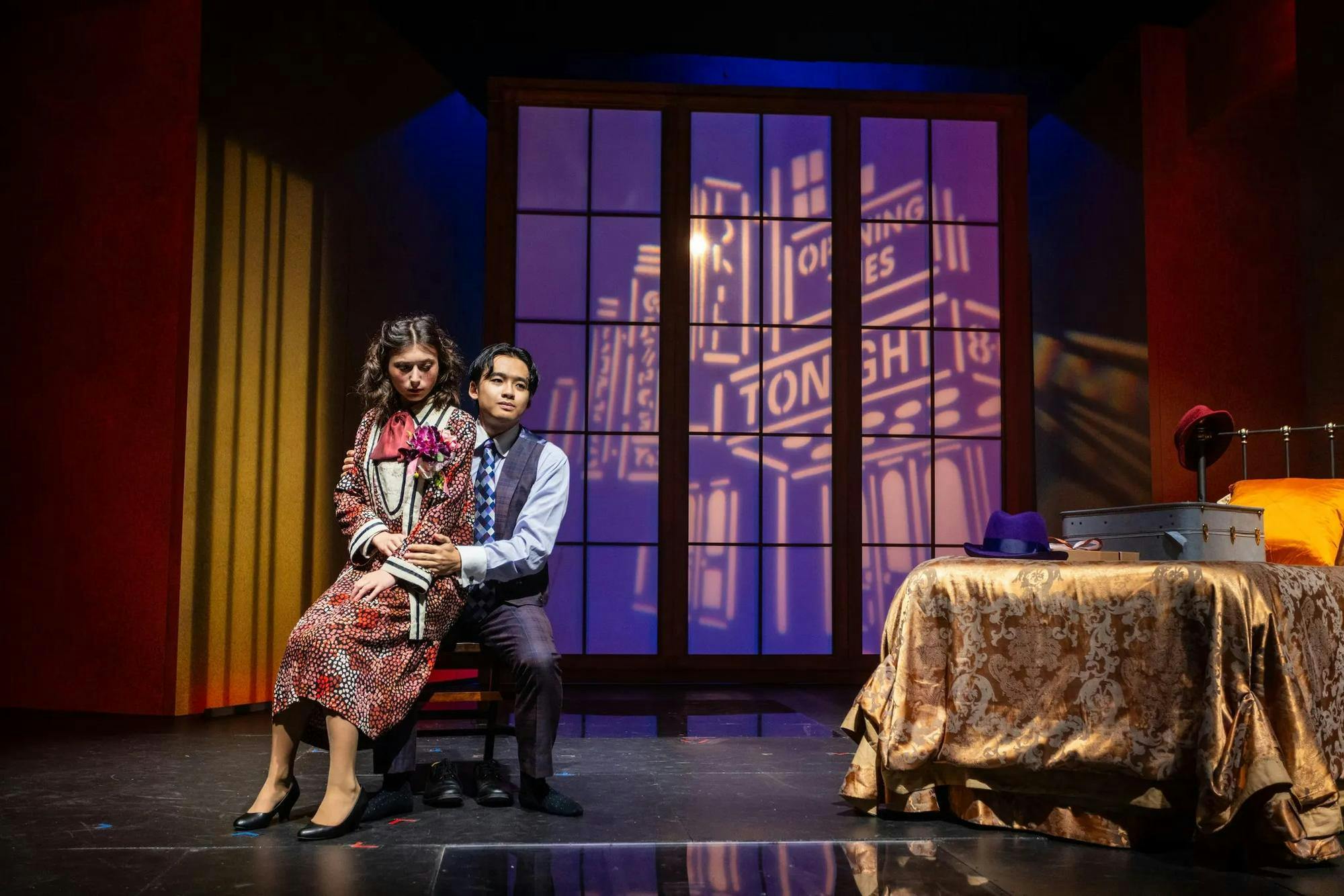 A young woman (actor) sits on the lap of a young man (actor)