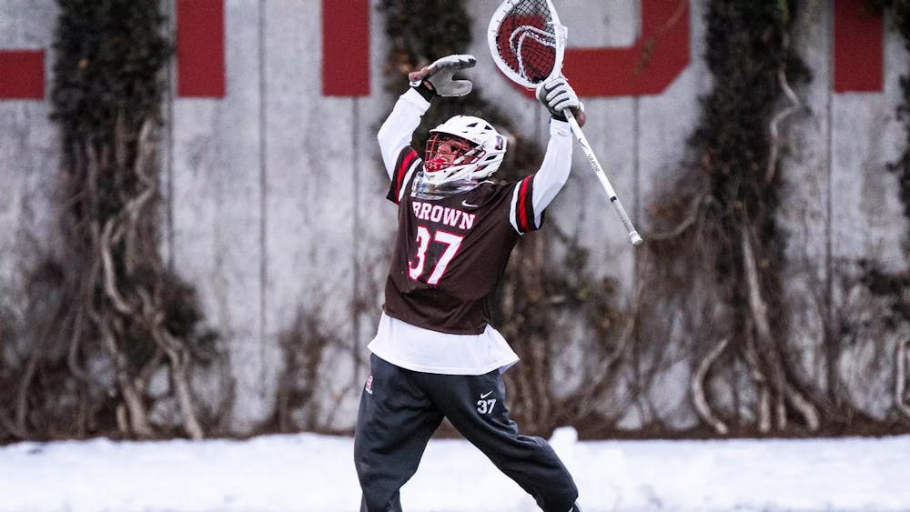 Photo of Brown Men’s Lacrosse player jumping, lifting his arms and lacrosse stick in the air.