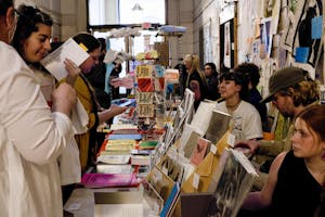 A photo of two women looking at an art vendor’s booth covered with colorful posters and cards.