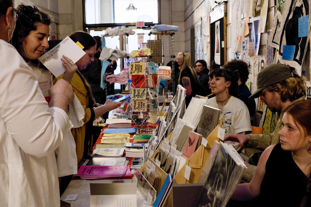 A photo of two women looking at an art vendor’s booth covered with colorful posters and cards.