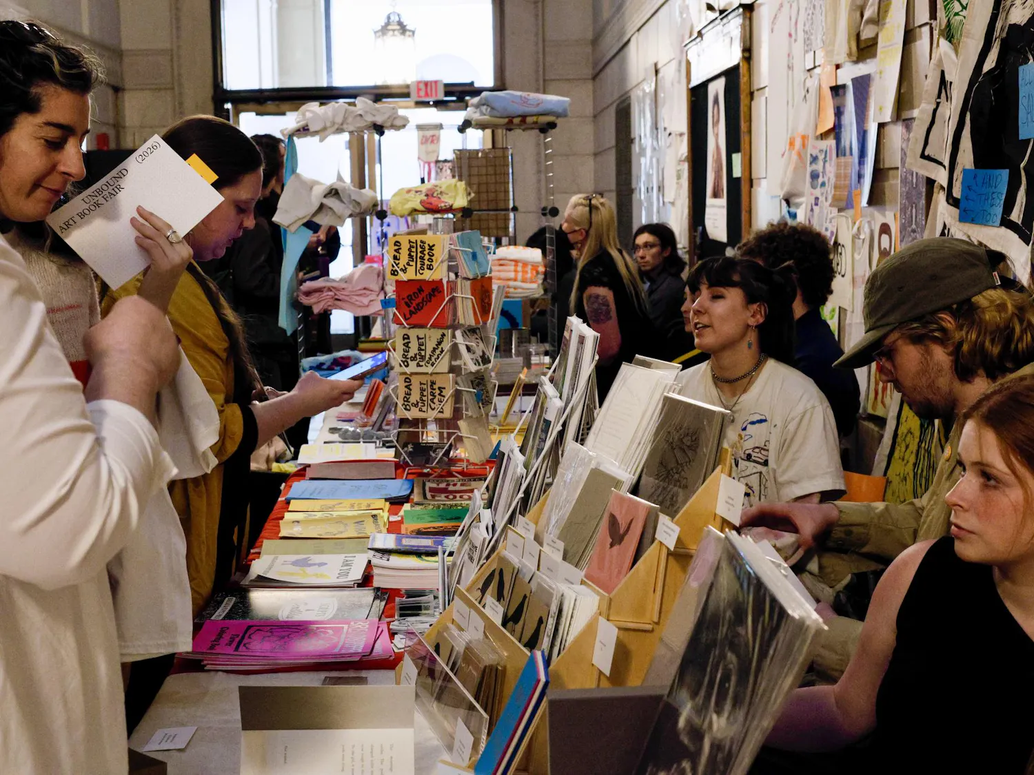 A photo of two women looking at an art vendor’s booth covered with colorful posters and cards.