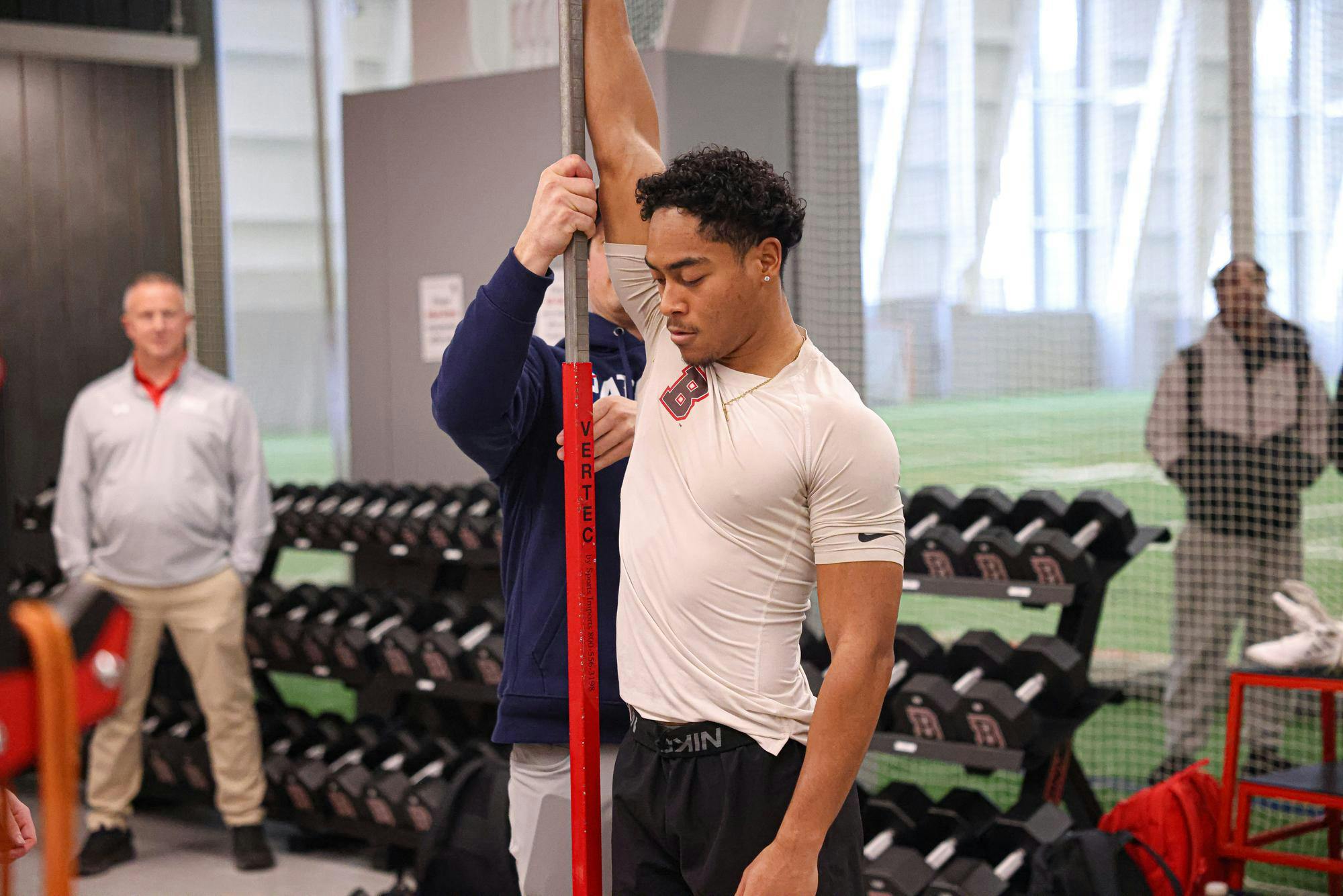 A man in a gray shirt stands with his left arm raised.