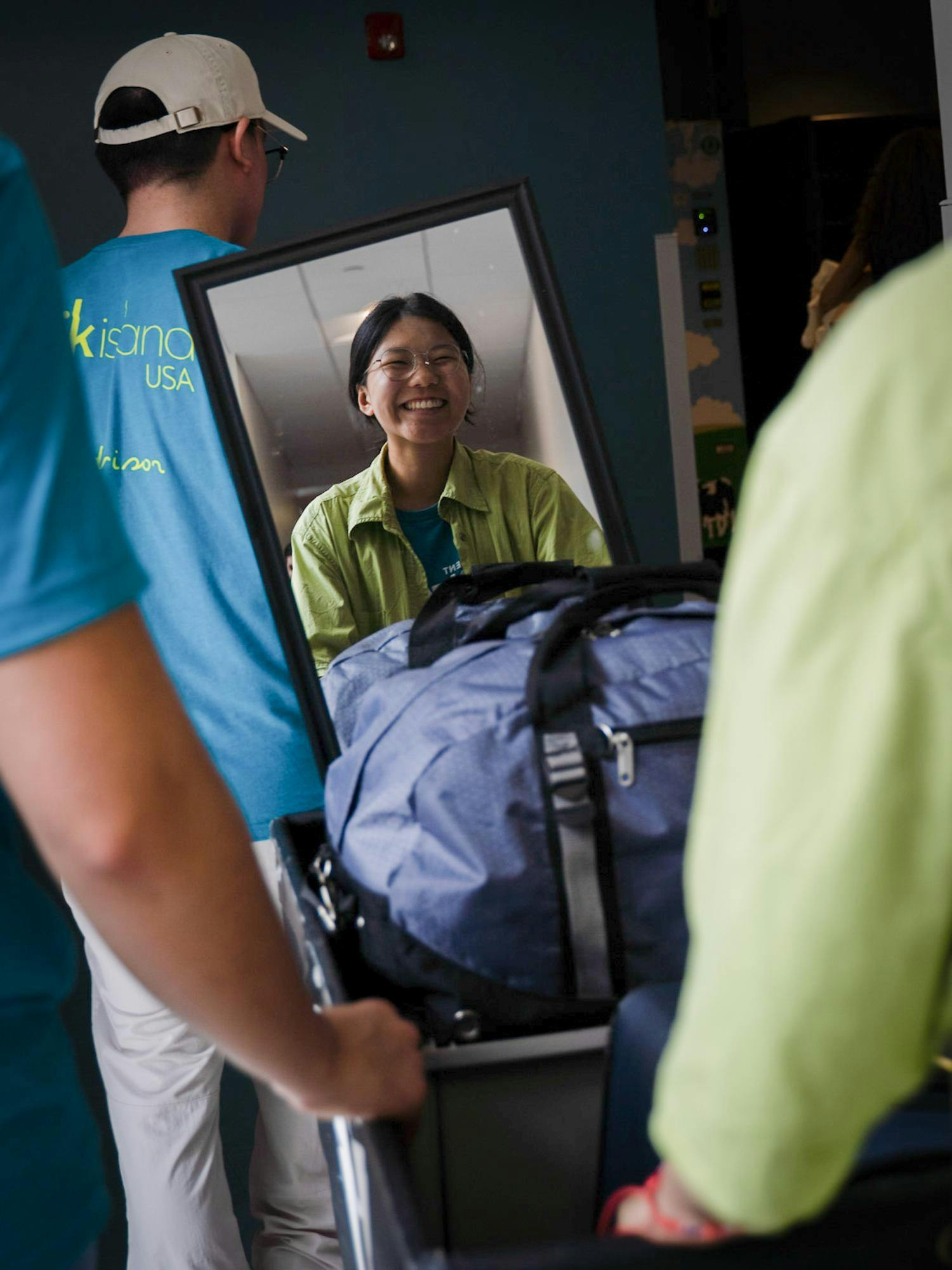 Photo of a move-in volunteer smiling through the reflection of a mirror as the volunteer helps push luggage.
