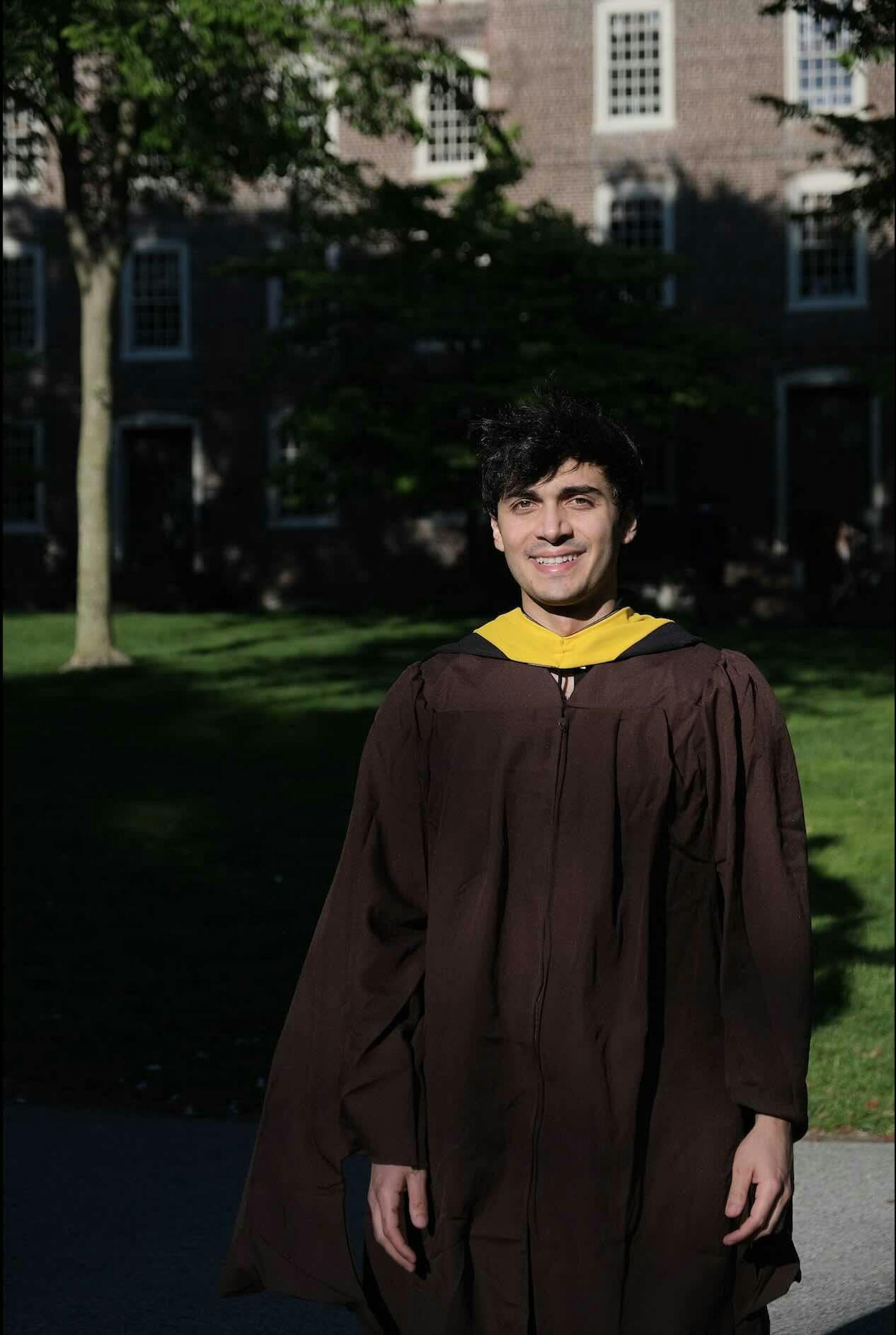 A student stands in a graduation gown on Brown's campus. 
