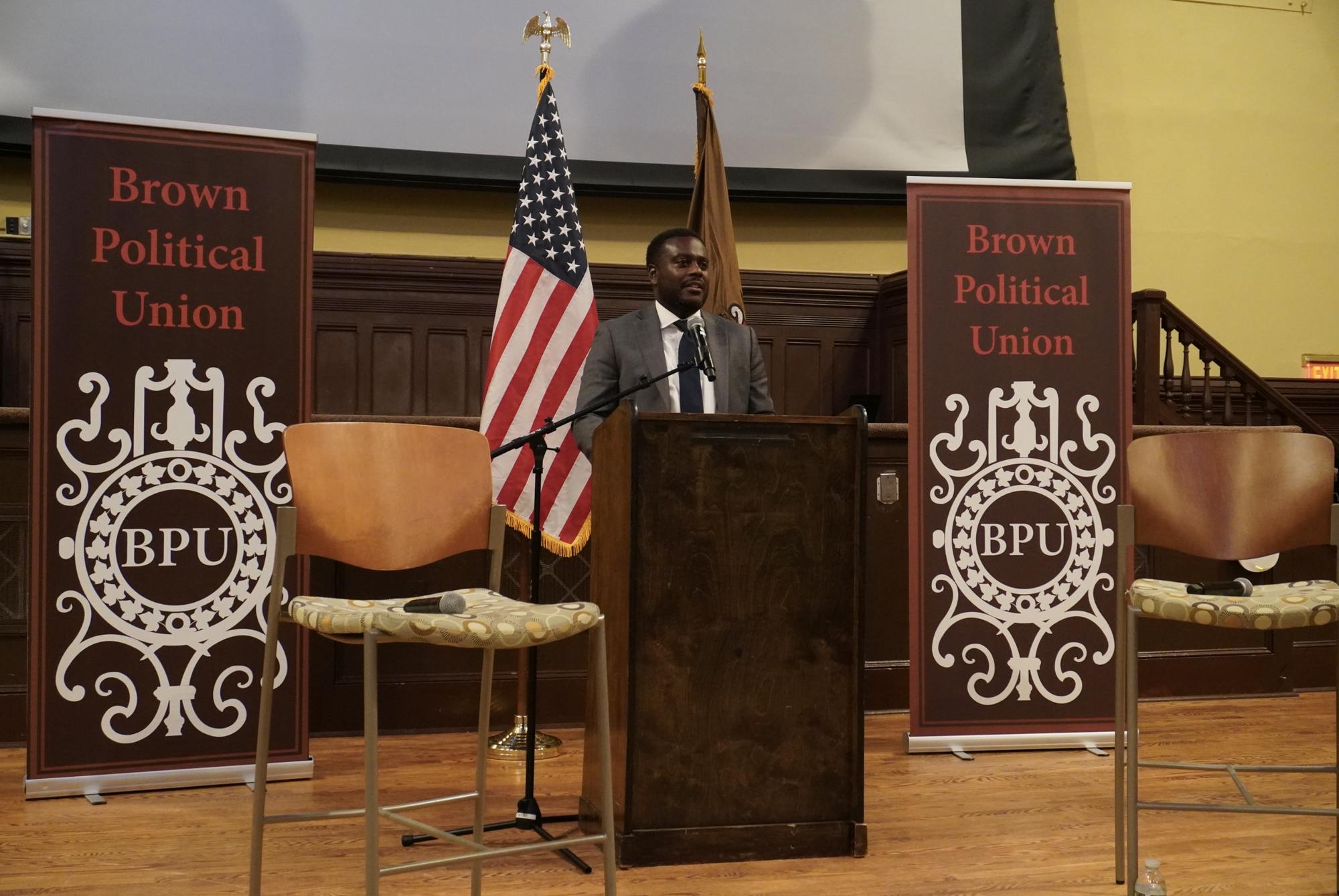 U.S. Representative Gabe Amo (D-R.I. 1) stands at a podium in Sayles Hall alongside Brown Political Union banners.