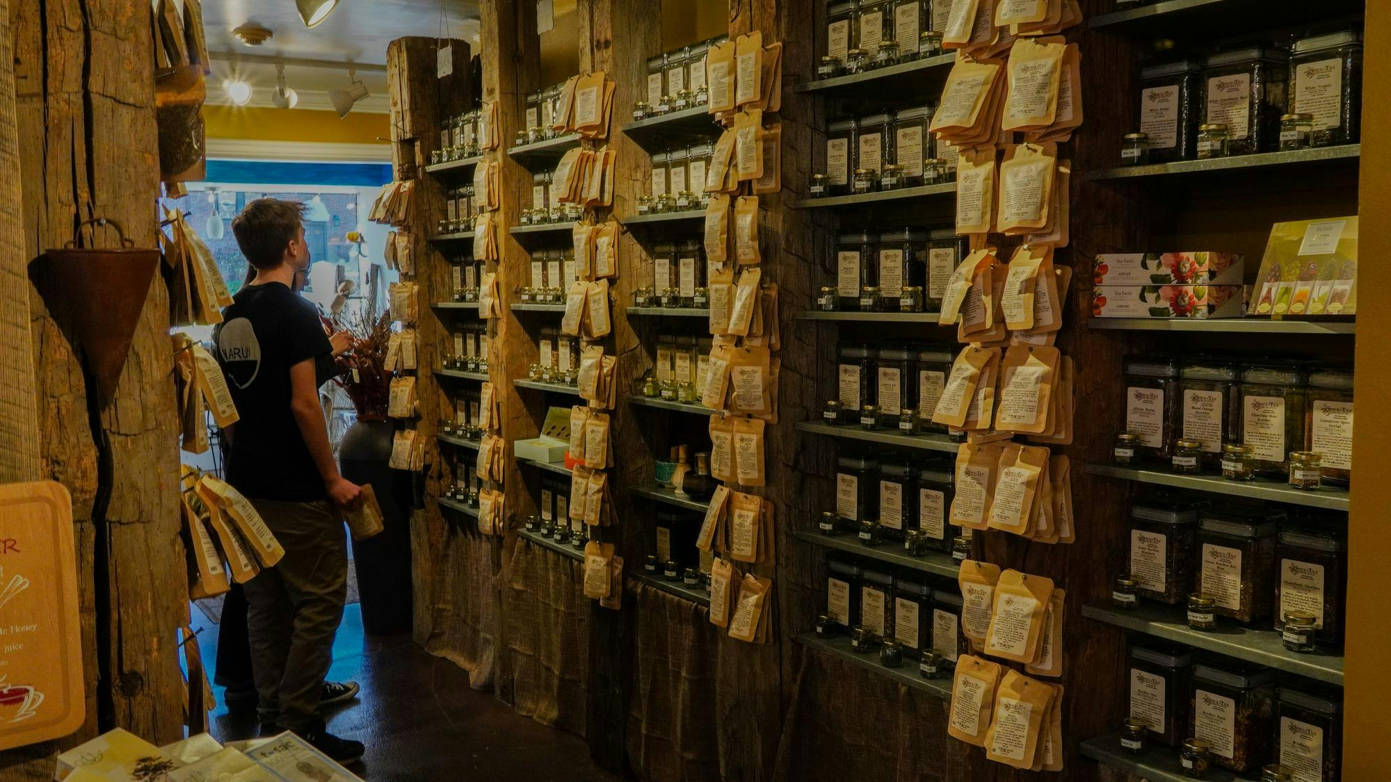 A person stands facing shelves of teas and packets hung off of wooden pillars 