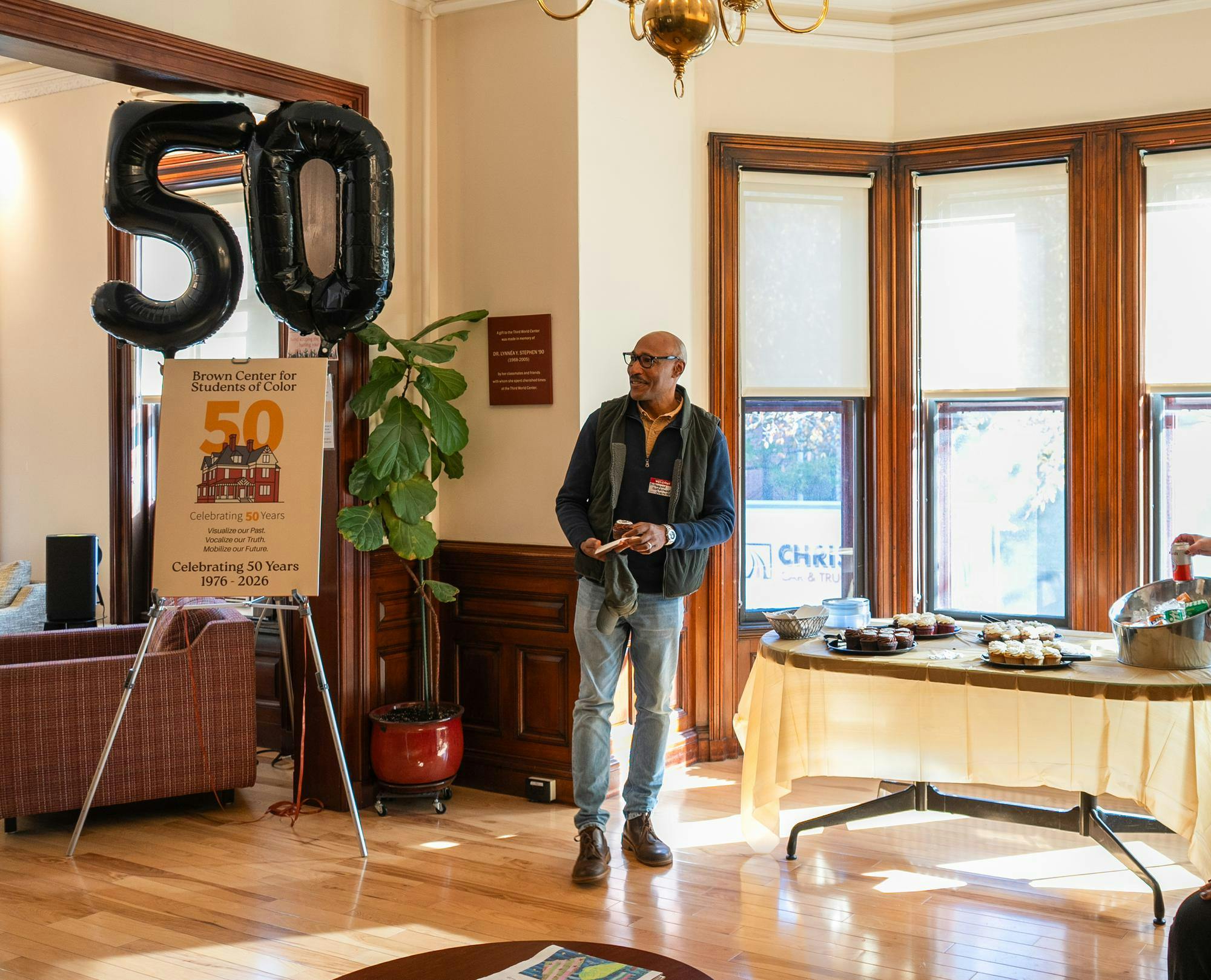 A photo of the 50th anniversary celebration on the first floor of the BSCS. There is a “5” and “0” balloon on top of a small poster board about the event in the left corner of the photo. There is a table with pastries and drinks as well. 