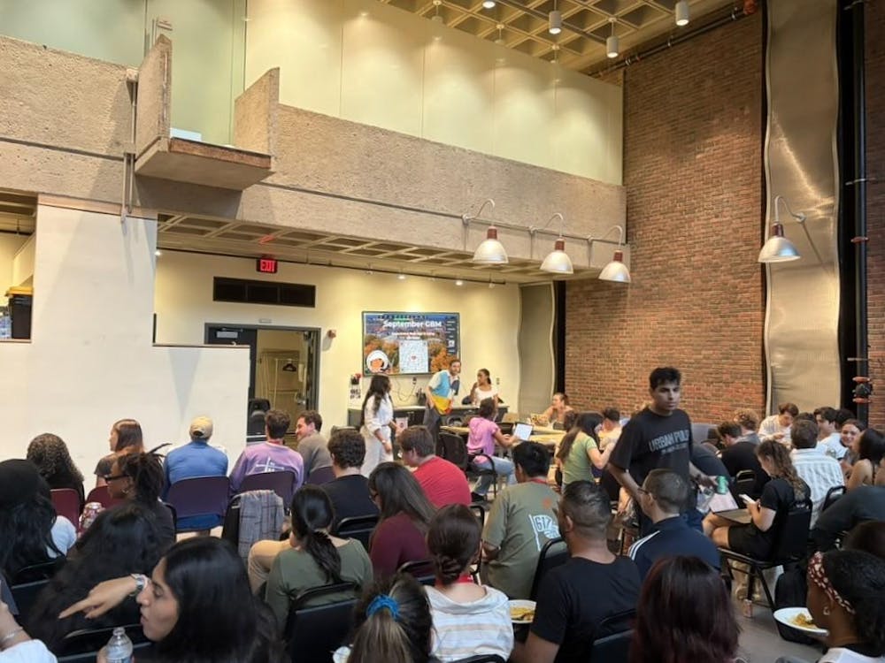 A photo shows a crowd of graduate students seated at a presentation in the Graduate Center.

