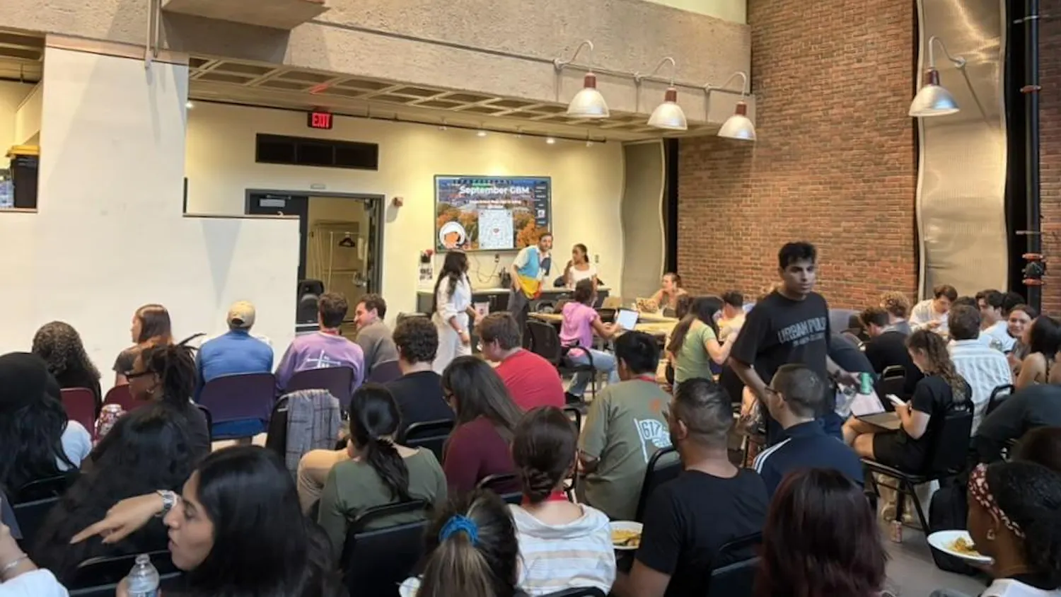 A photo shows a crowd of graduate students seated at a presentation in the Graduate Center.
