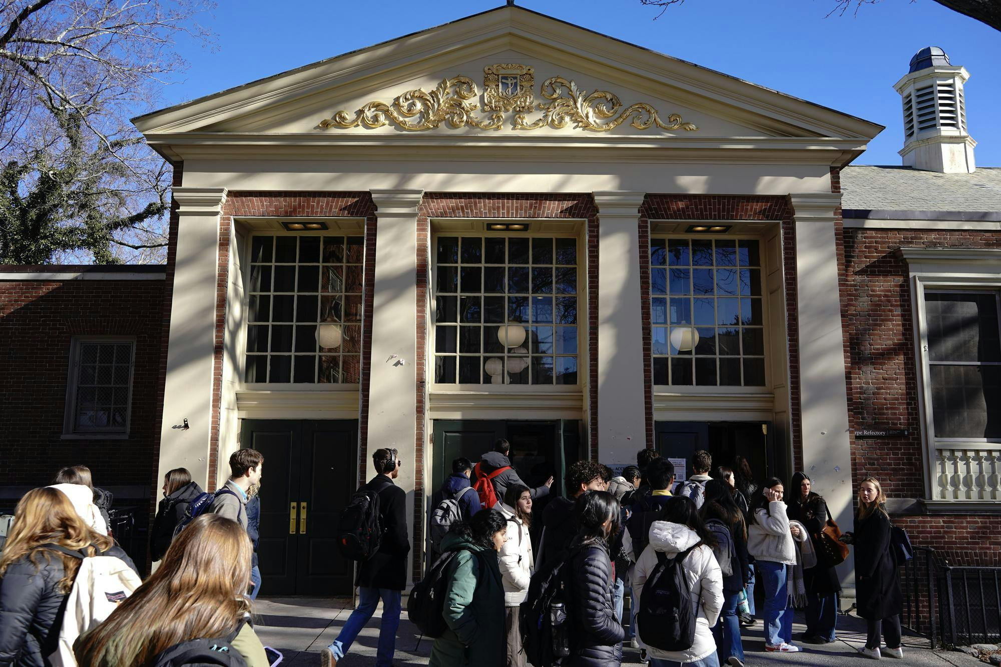 A photo showing the outside of Sharpe Refectory dining hall with people walking in and out of the front doors. 