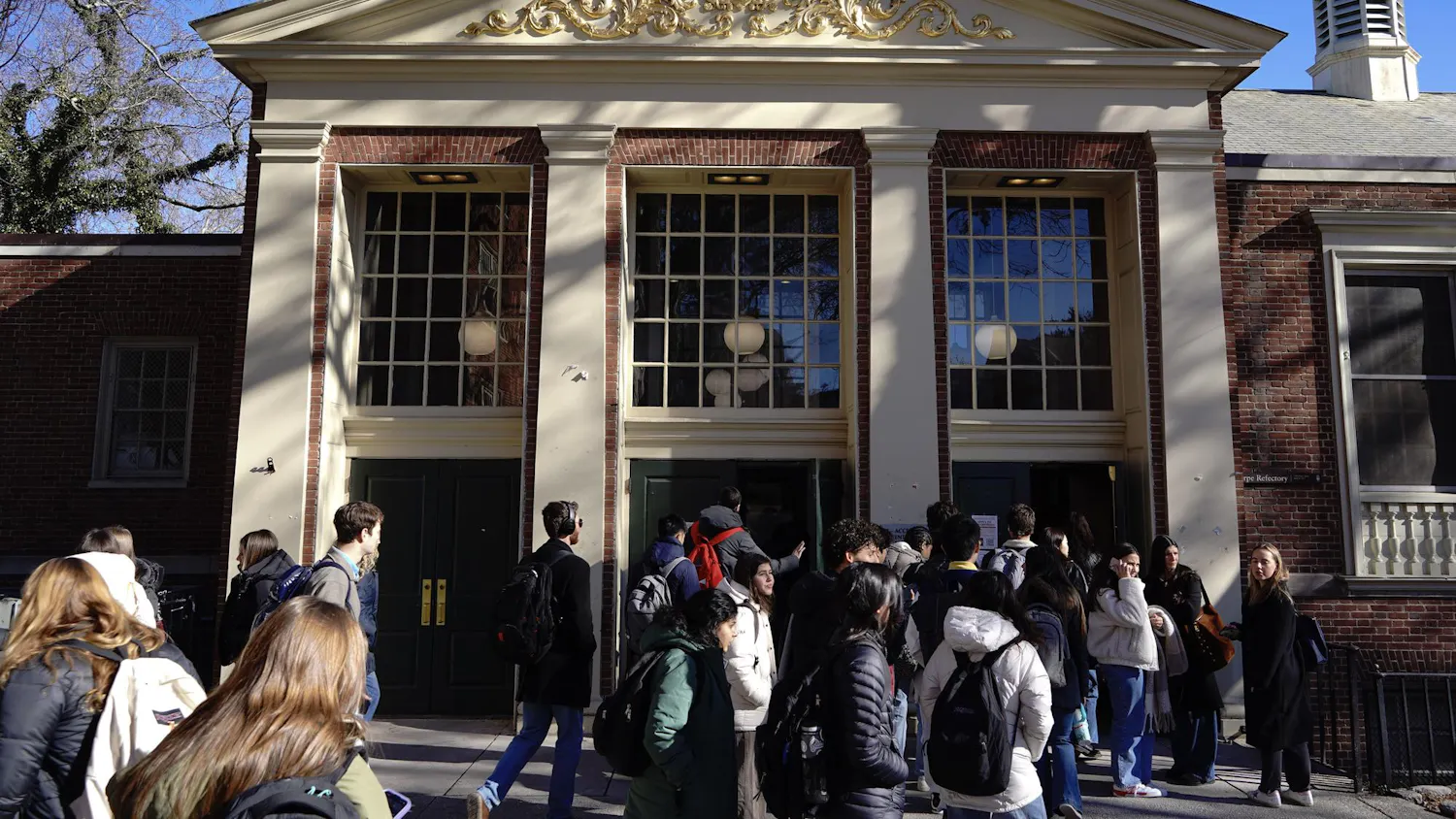 A photo showing the outside of Sharpe Refectory dining hall with people walking in and out of the front doors.