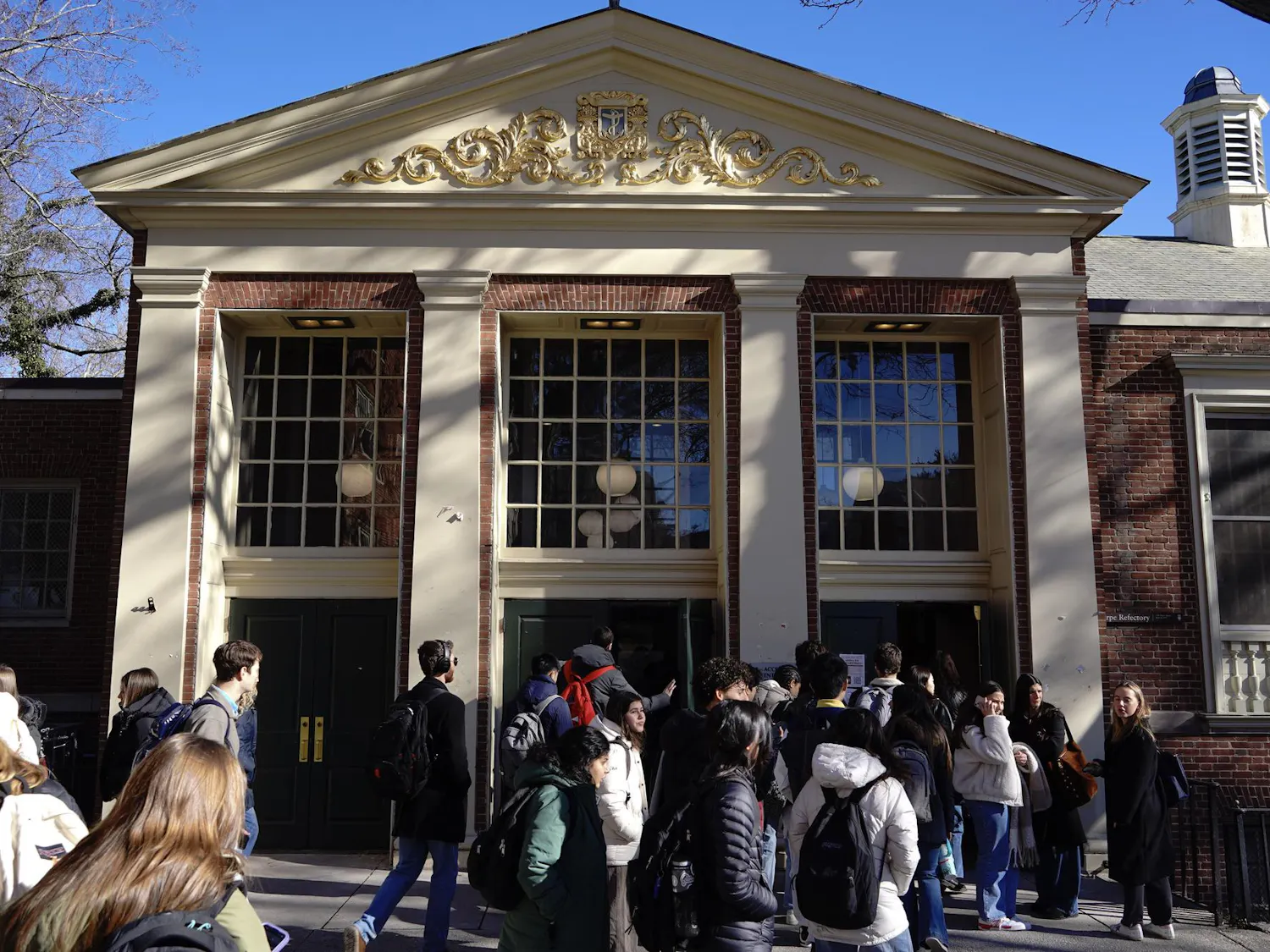 A photo showing the outside of Sharpe Refectory dining hall with people walking in and out of the front doors.
