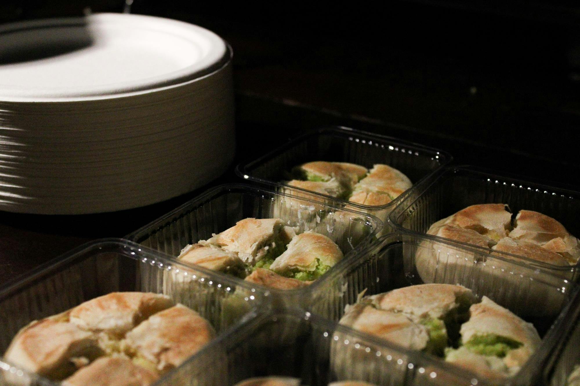 Photo of five pastries with green filling on the inside, all sitting inside plastic boxes. A stack of white plates sits at the back of the photo.